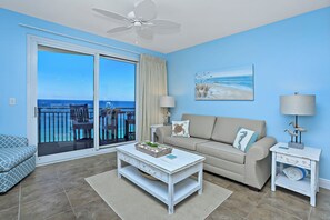 A living room with a sofa, a coffee table, and a view of the ocean through a sliding glass door. - Sterling Breeze 2001 (Panama City Beach)