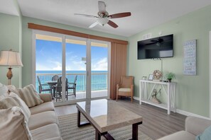 A living room with a view of the ocean, a ceiling fan, a television, and a sign with beach rules. - Seychelles Beach Resort 901 - 99987 (Panama City Beach)