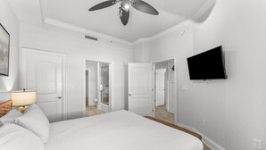A hotel room with a bed, a ceiling fan, a TV mounted on the wall, and a door leading to another room. - Sol Mate Unit C304 (Santa Rosa Beach)