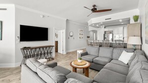 A modern living room with a grey sectional sofa, a flat-screen TV, and a ceiling fan. - Sol Mate Unit C304 (Santa Rosa Beach)