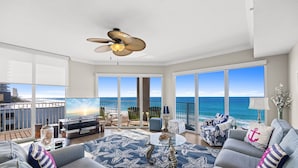 A modern living room with a large TV, comfortable seating, a ceiling fan, and a balcony with a view of the ocean. - Tidewater 317 (Panama City Beach)