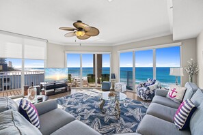 Een moderne woonkamer met een grote televisie, comfortabele zithoek, een plafondventilator en een balkon met uitzicht op zee.