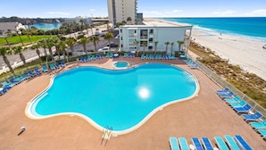 A swimming pool with lounge chairs, a beach, and a tall building in the background. - Tidewater 317 (Panama City Beach)