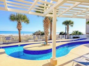 A pool area with a white pergola, palm trees, and a view of the ocean.