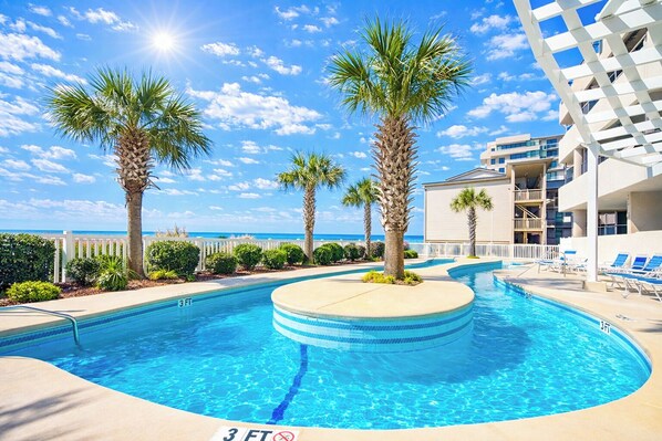 A swimming pool with a 3 FT depth marker, surrounded by palm trees and a building with balconies.
