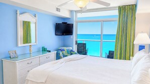 Ein Schlafzimmer mit einem Bett, einer Kommode, einem Fernseher, einem Deckenventilator und Blick aufs Meer.