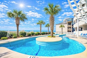 A swimming pool with palm trees, a white fence, and a building with balconies. - Bluewater Keyes 903 (North Myrtle Beach)