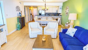 Ein Wohnzimmer mit einem blauen Sofa, zwei gestreiften Sesseln, einem Holztisch und einem Essbereich mit einer Chandelier.