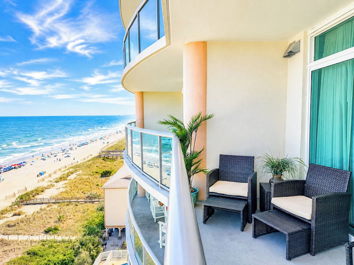 A balcony with wicker furniture overlooking a beach.