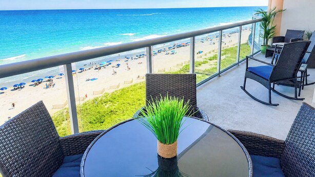 Ein Balkon mit Korbmöbeln, einem Glastisch und Blick auf Strand und Meer.
