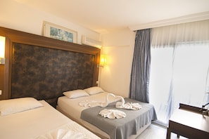 A hotel room with two beds, a wooden headboard, a wall-mounted air conditioner, a bedside lamp, and a window with curtains.