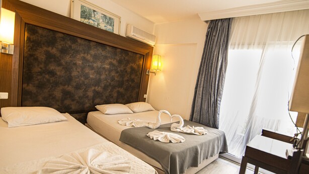 A hotel room with two beds, a desk, and a window with curtains. - Famous Hotel Marmaris (Marmaris)