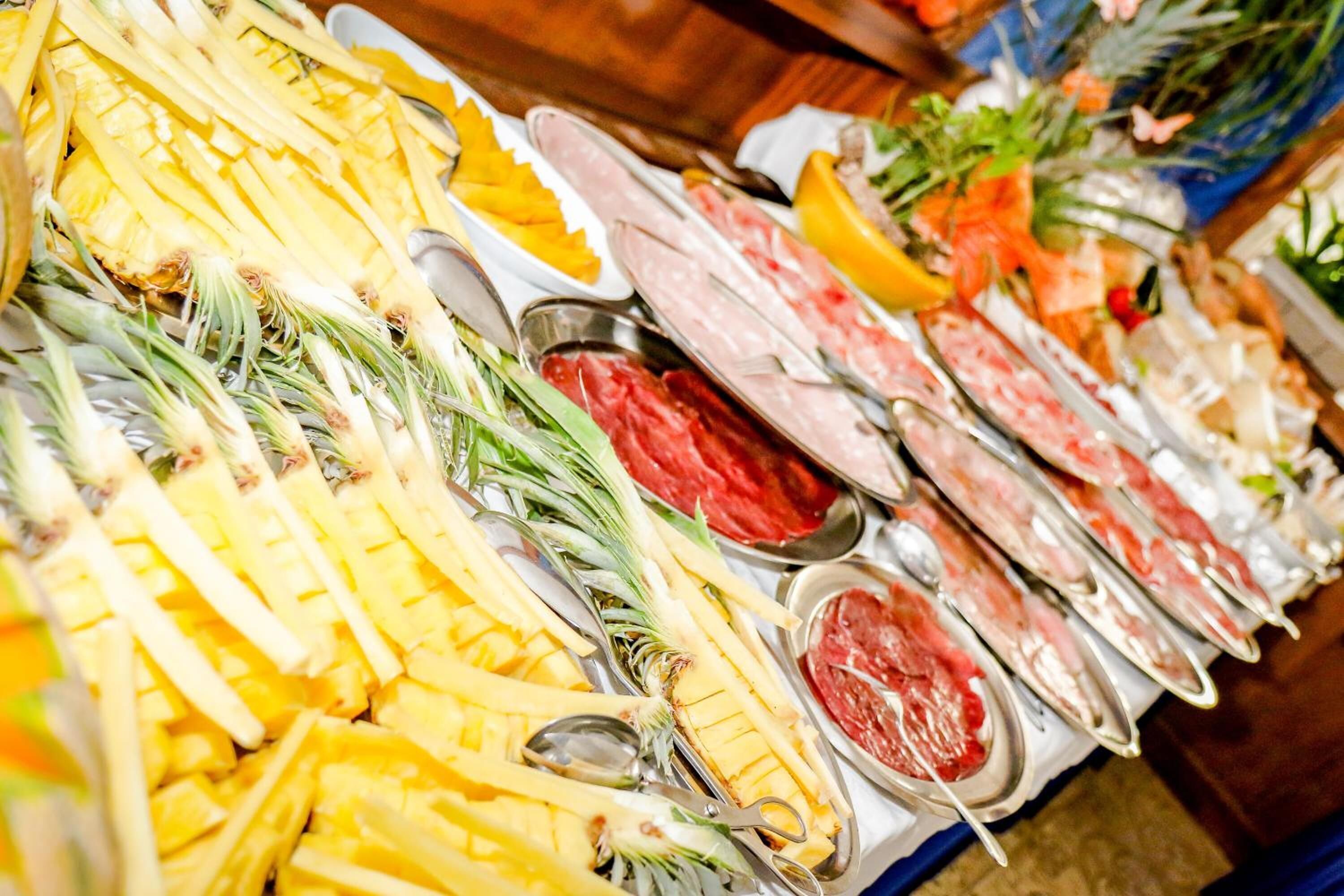 Un bufé con diversos alimentos, incluyendo piña, carne y otros platos.