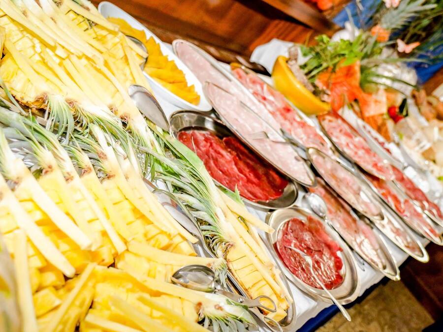 Un bufé con diversos alimentos, incluyendo piña, carne y otros platos.