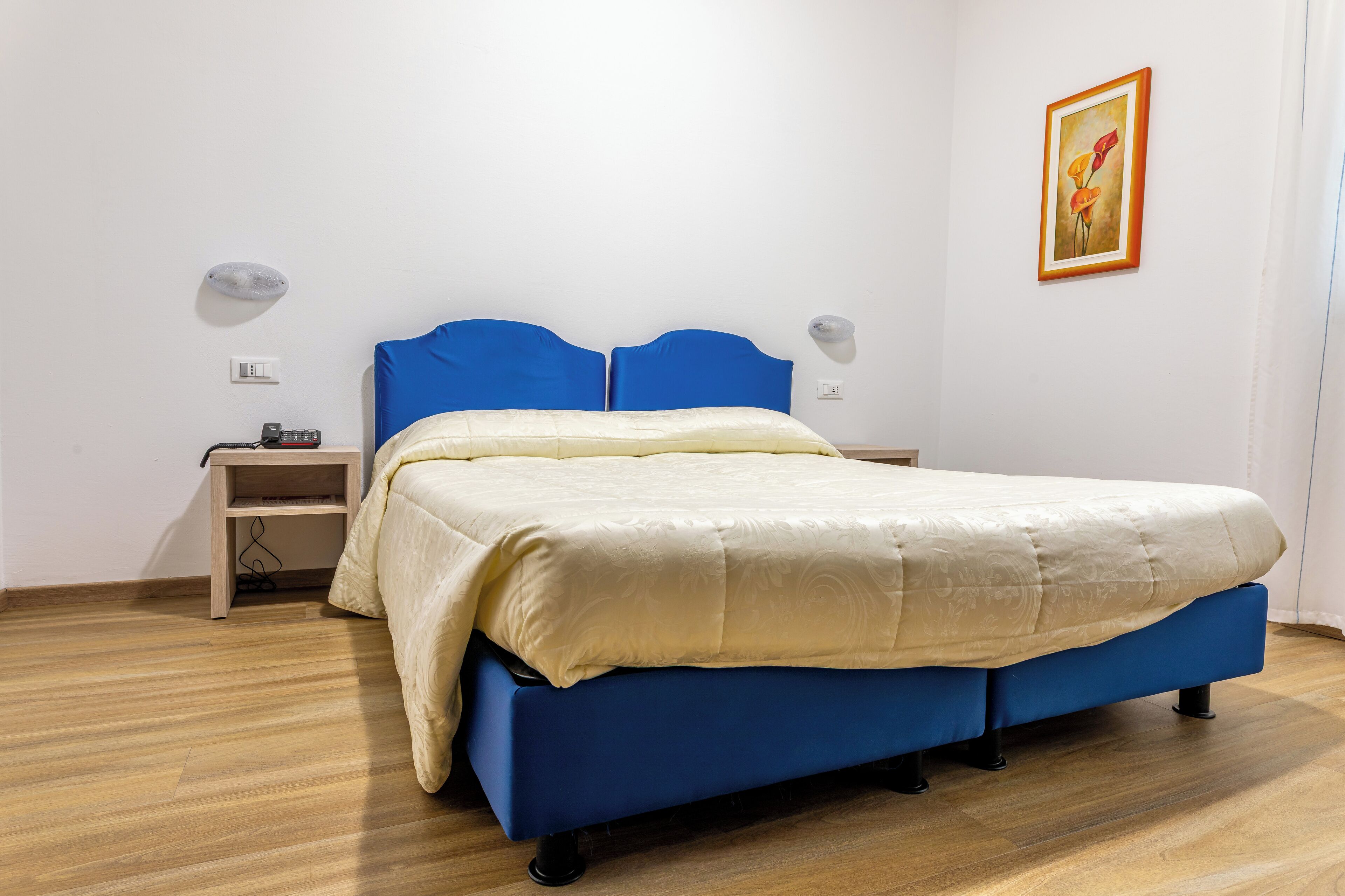 A bedroom with a blue bed, a wooden nightstand, and a wall-mounted lamp.