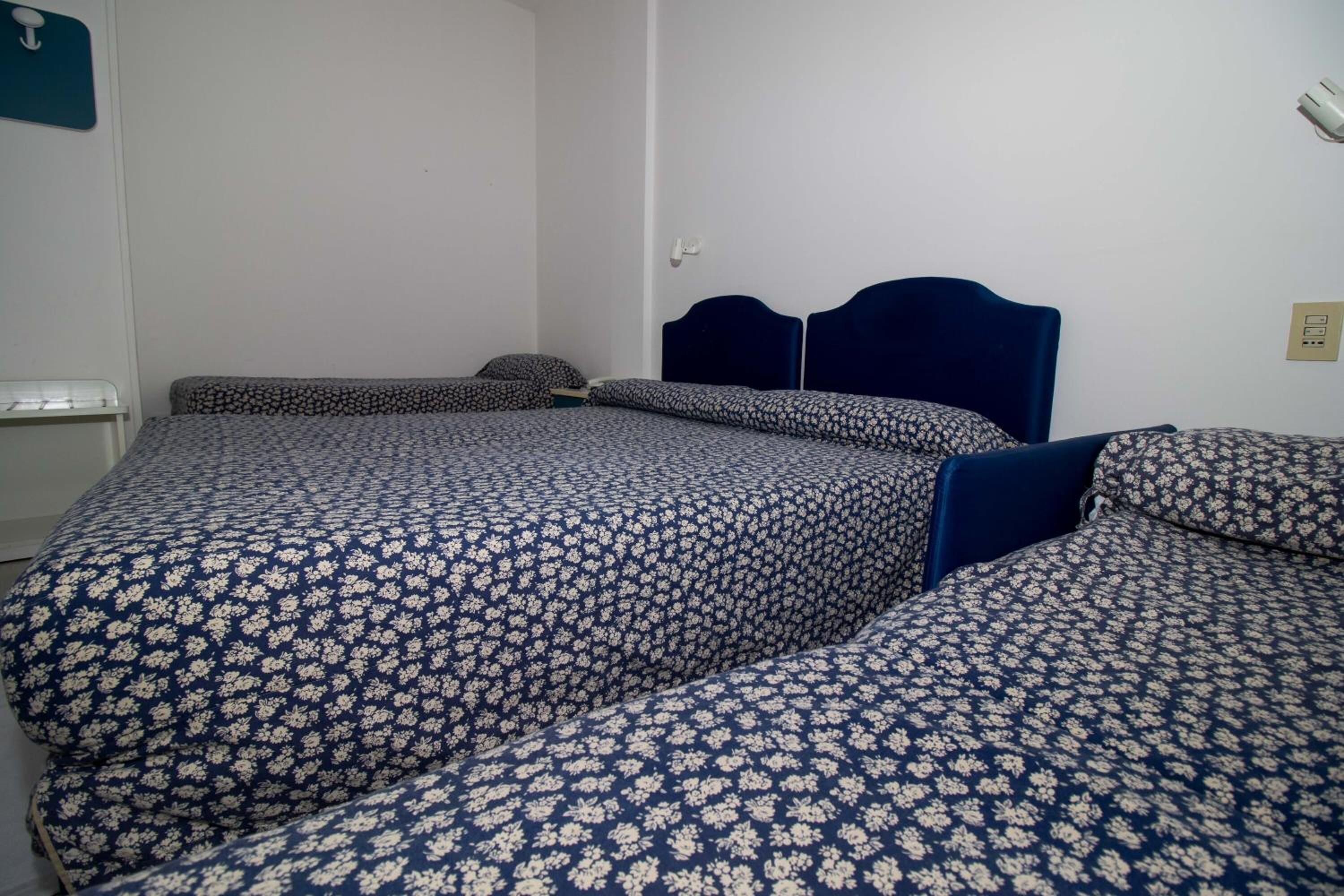 A room with two beds, each with a dark blue headboard and floral-patterned bedding.