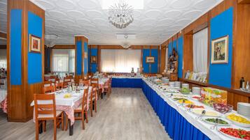 Une salle de banquet avec une longue table recouverte d’une nappe bleue, entourée de chaises en bois.