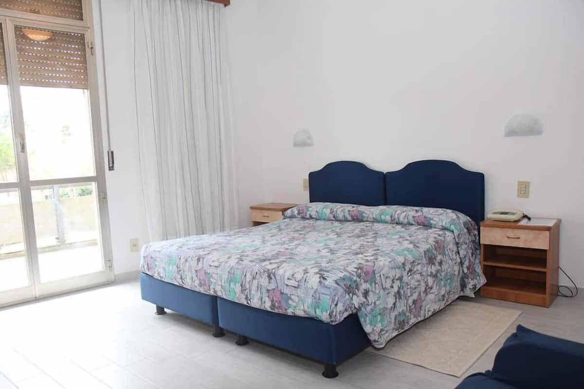 A bedroom with a bed, a nightstand, a lamp, and a window with curtains.