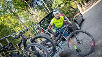 A person sitting on a bicycle with a rack, parked on a street with trees in the background.