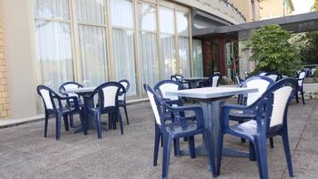 Outdoor seating with tables and chairs, a building with large windows, and a covered area.