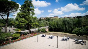 A spacious outdoor patio with tiled flooring, surrounded by lush greenery and flowering plants. - Hotel Cristallo (Riolo Terme)