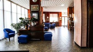 A spacious lobby with a patterned floor, blue seating, and a central plant arrangement. - Hotel Cristallo (Riolo Terme)