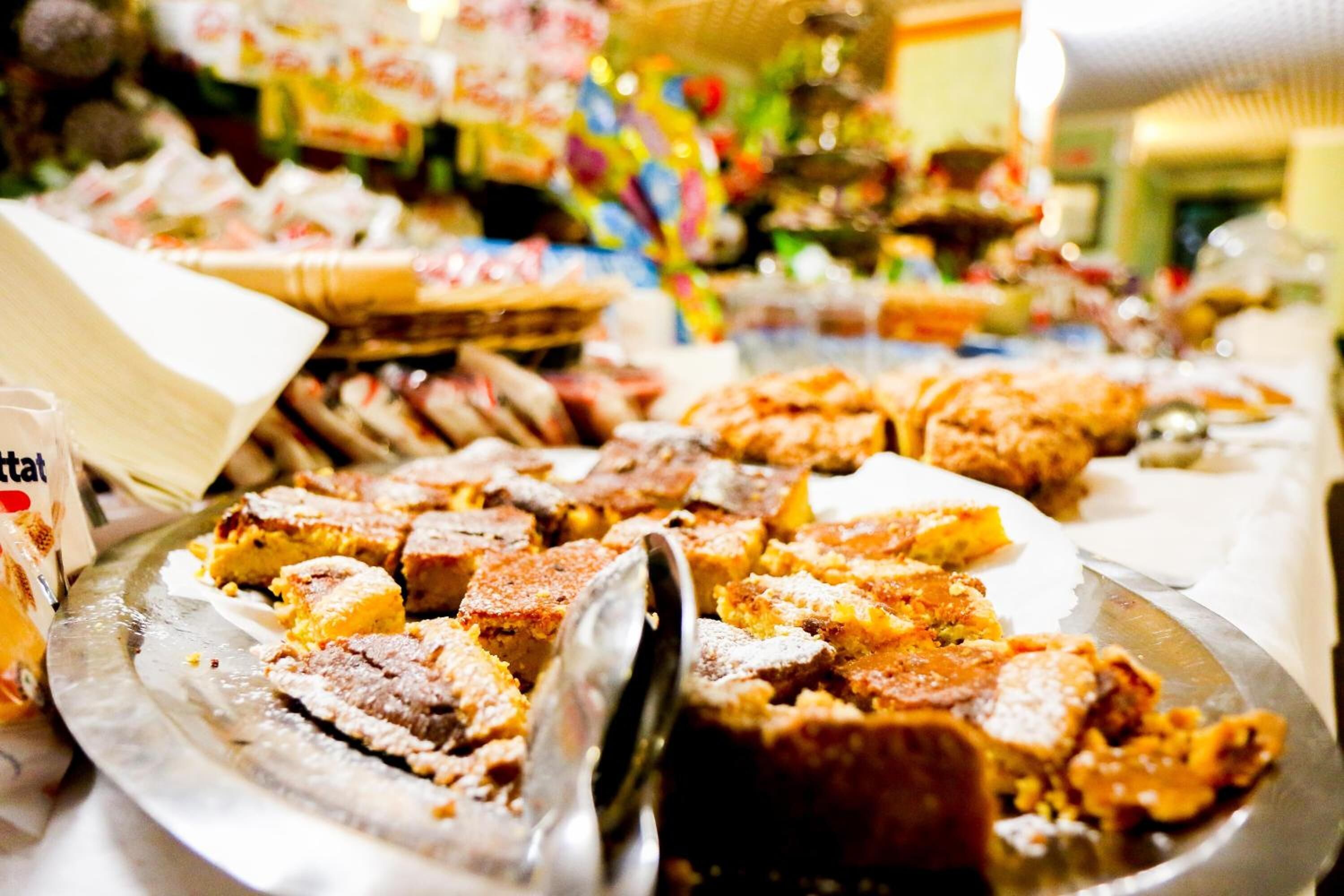 A buffet with various food items, including a large platter of bread and a container of what appears to be a dessert or sweet dish.