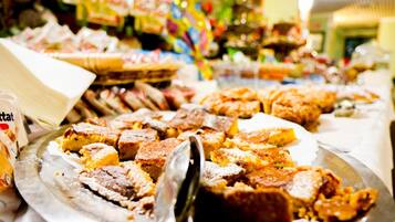 A buffet with various food items, including a large platter of bread and a container of what appears to be a dessert or sweet dish.