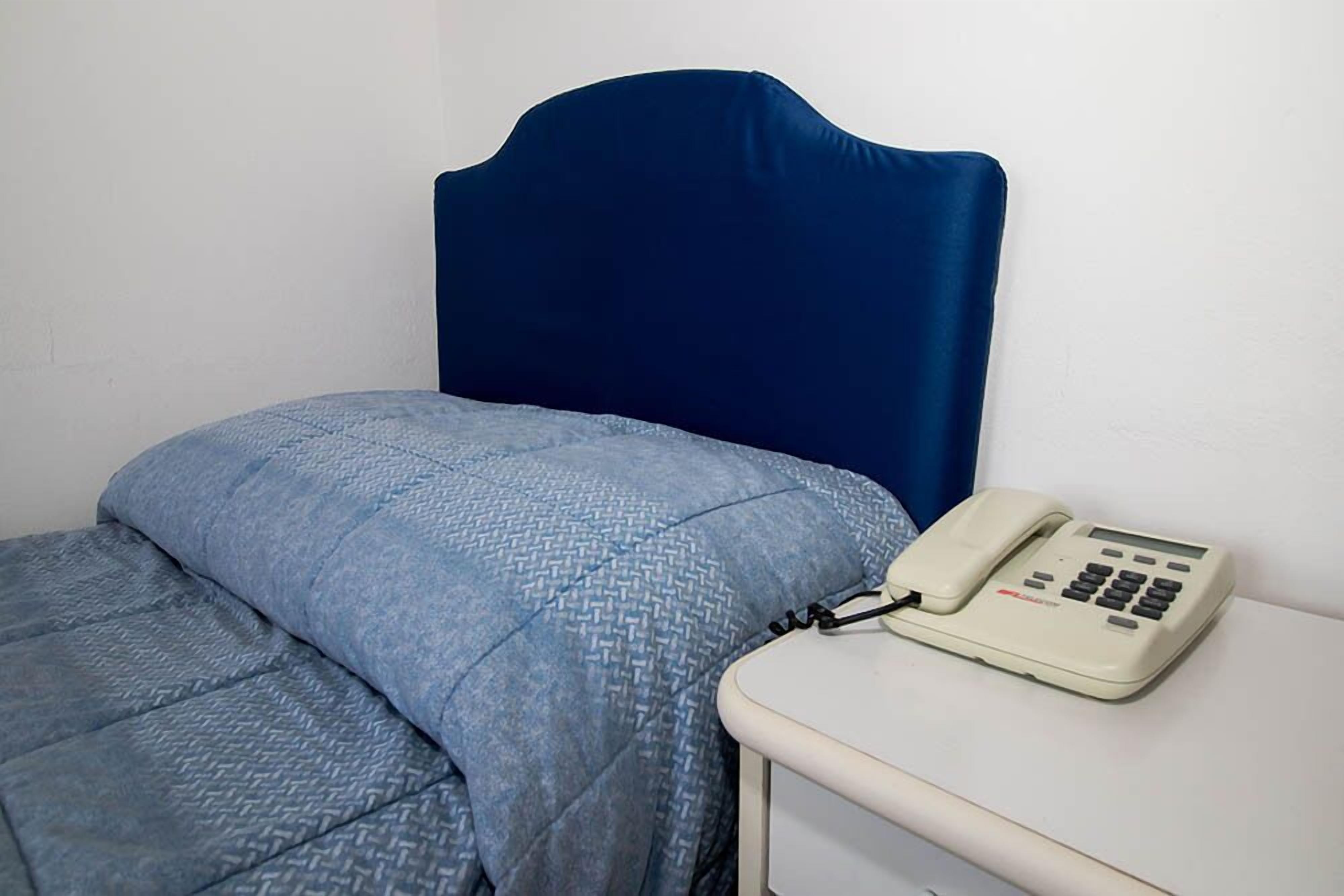 A bed with a blue headboard and a patterned blue blanket. A white bedside table with a telephone is visible.