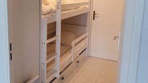 A narrow hallway with bunk beds, a door, and a ceiling light fixture.