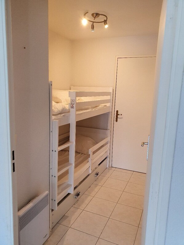 A narrow hallway with bunk beds, a door, and a ceiling light fixture.