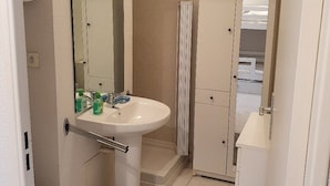 A bathroom with a white sink, mirror, and toilet. There is a shower curtain and a small trash bin.