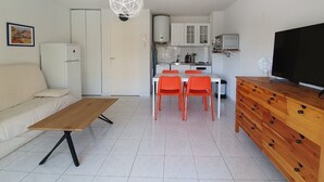 A compact living space with a kitchenette, a dining area, a sofa, a TV, and a wooden dresser.