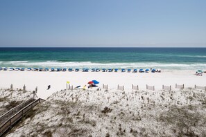 A beach with a wooden boardwalk leading to the shore, sandy dunes, and beach umbrellas.