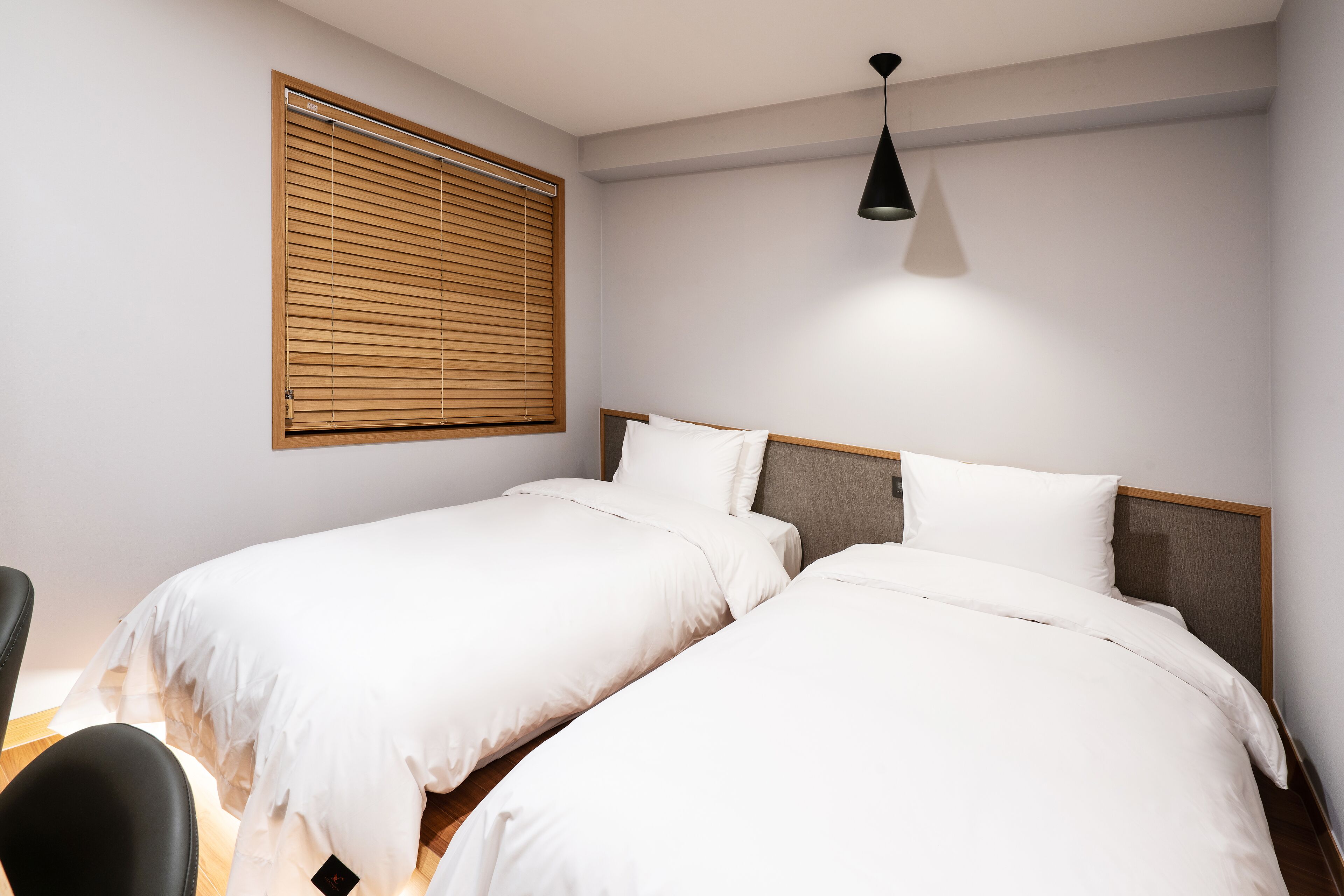 Un dormitorio con dos camas, cabeceros de madera, una ventana con persianas y una lámpara colgante.