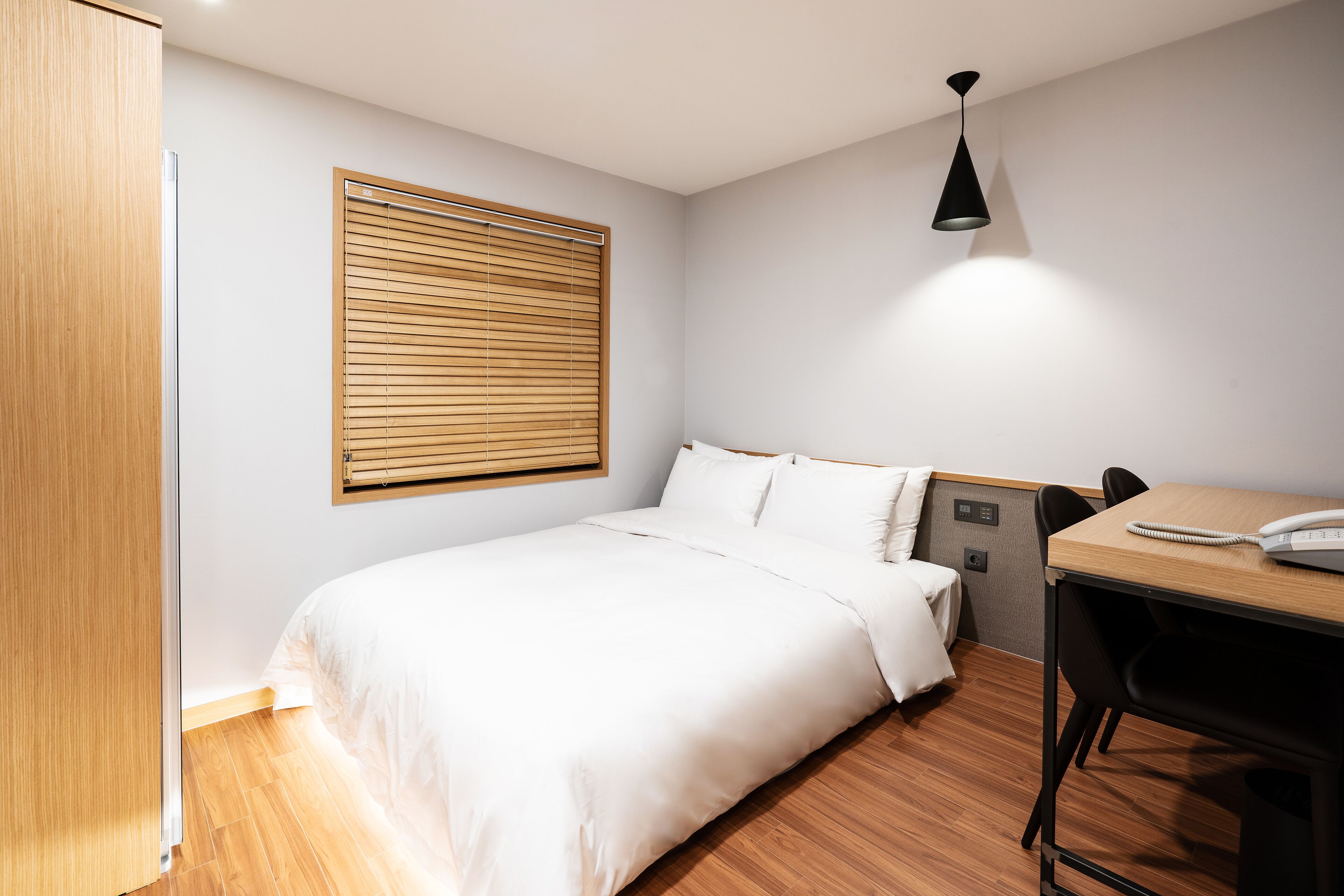 A neatly arranged hotel room with a bed, a desk, and a chair.