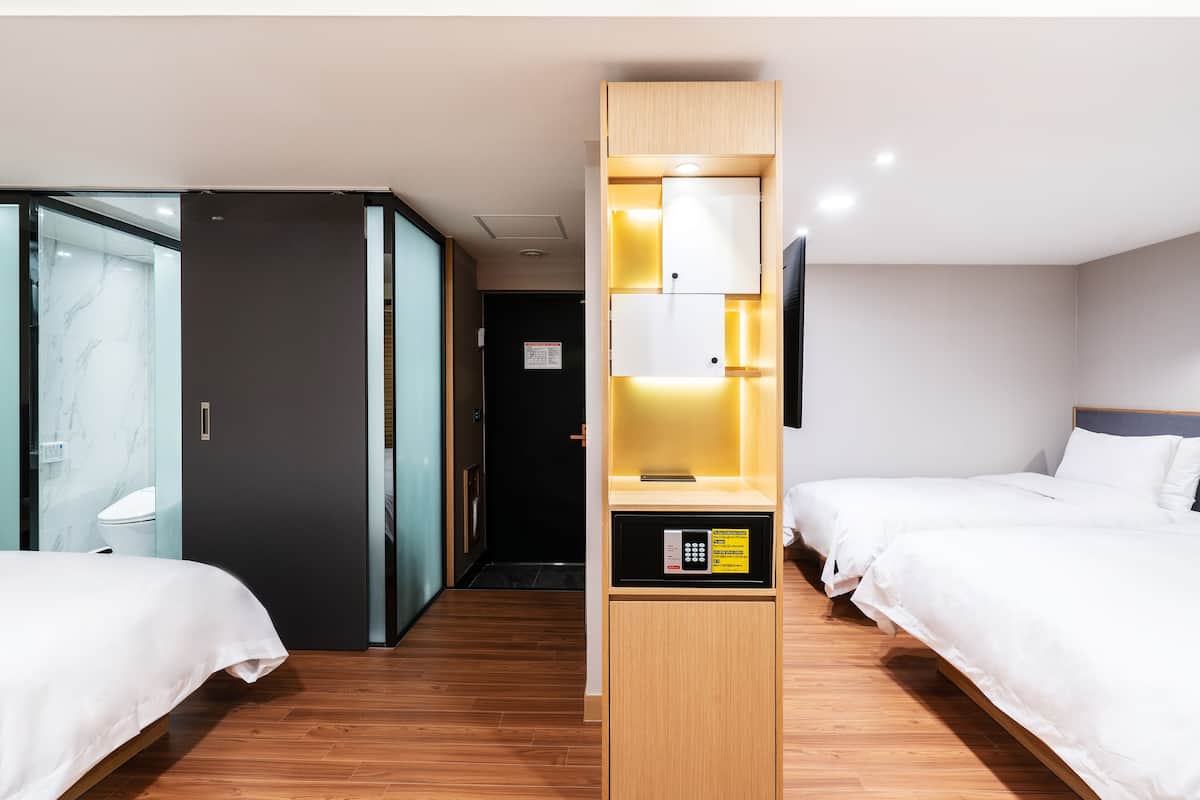 A hotel room with two beds, a minibar, a mirror, and a door leading to a bathroom.