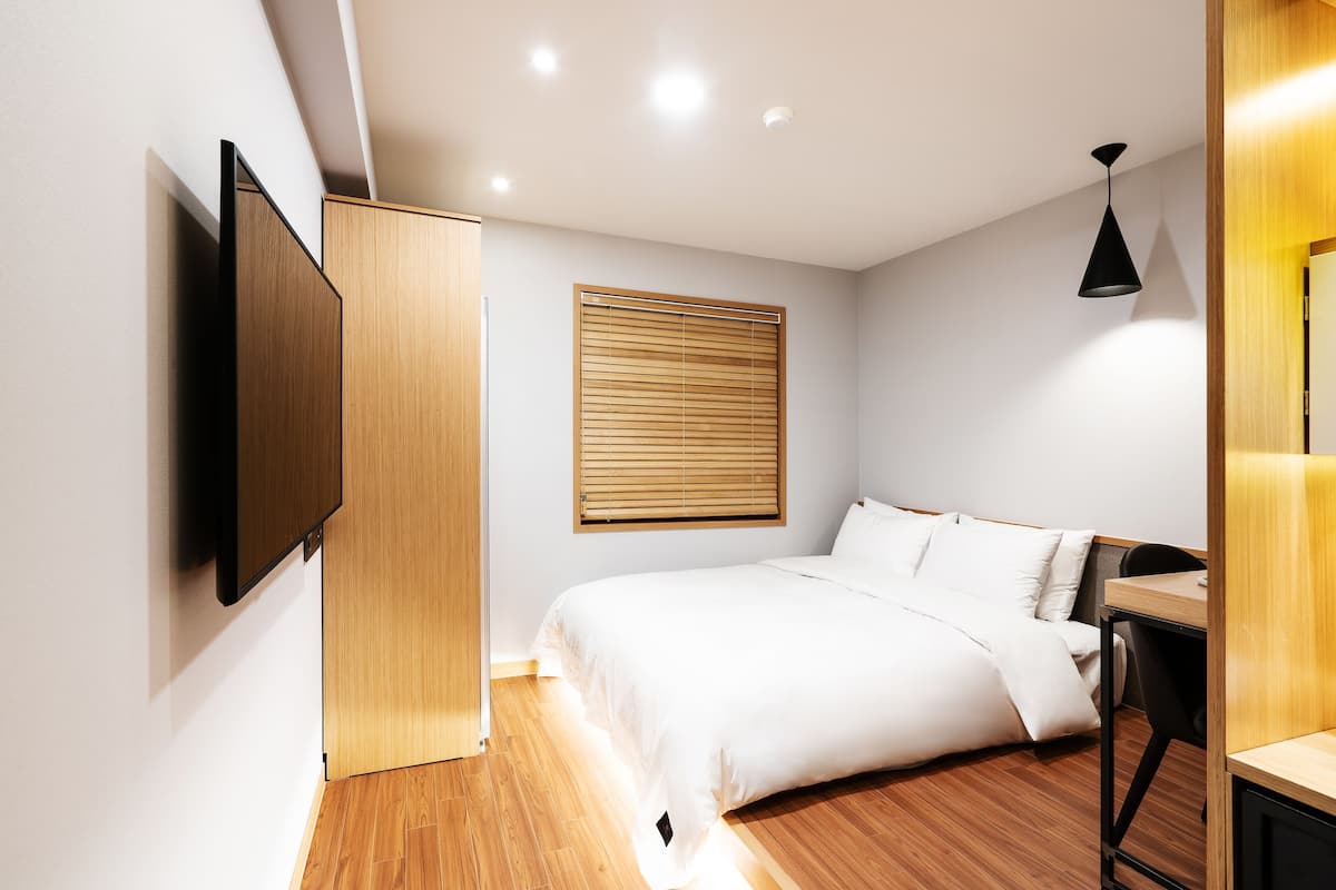 A modern bedroom with a bed, wooden flooring, a wall-mounted TV, and a ceiling light fixture.