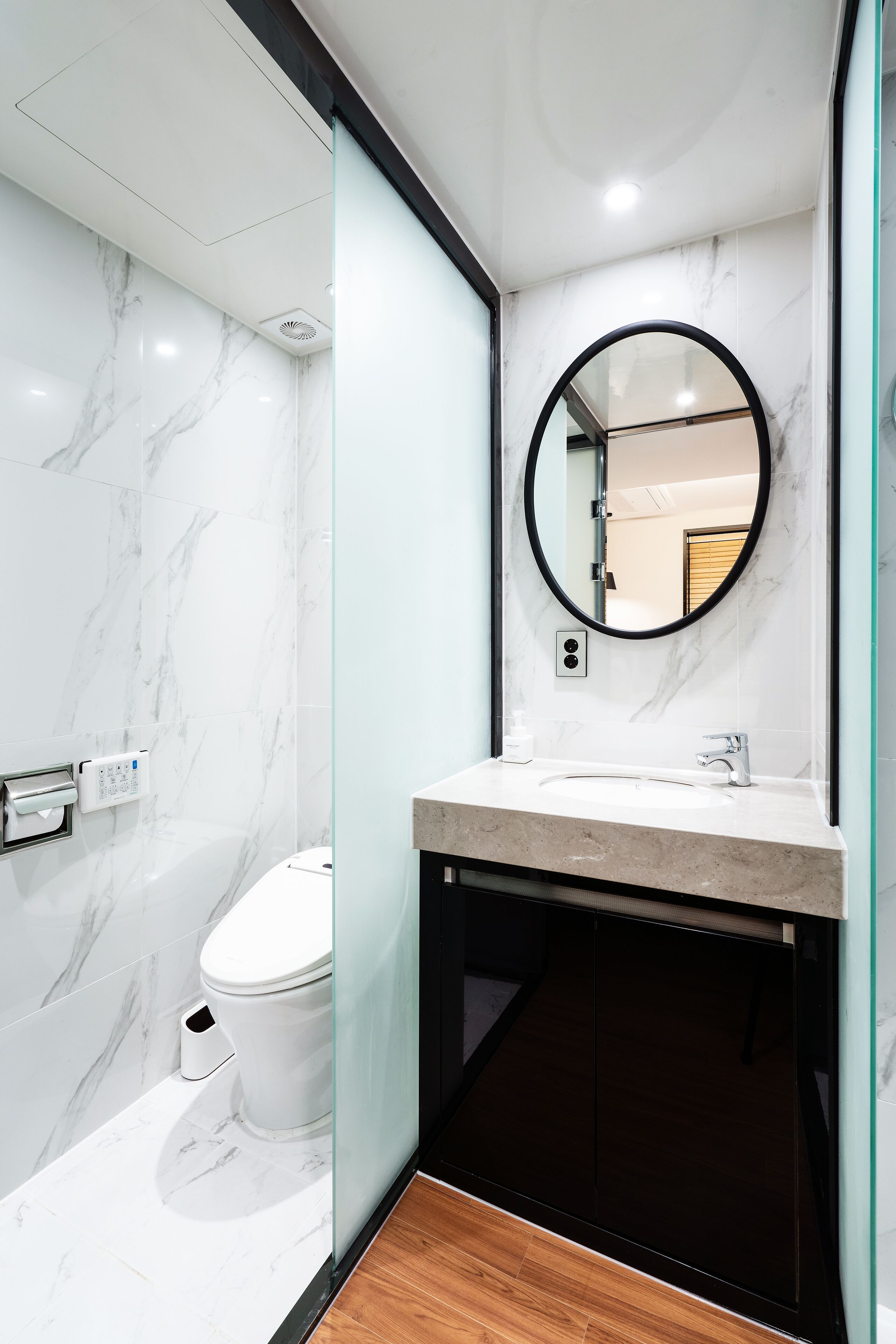 A modern bathroom with a marble floor, a toilet, a sink with a mirror, and a shower area.