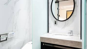 A modern bathroom with a marble floor, a toilet, a sink with a mirror, and a shower area.