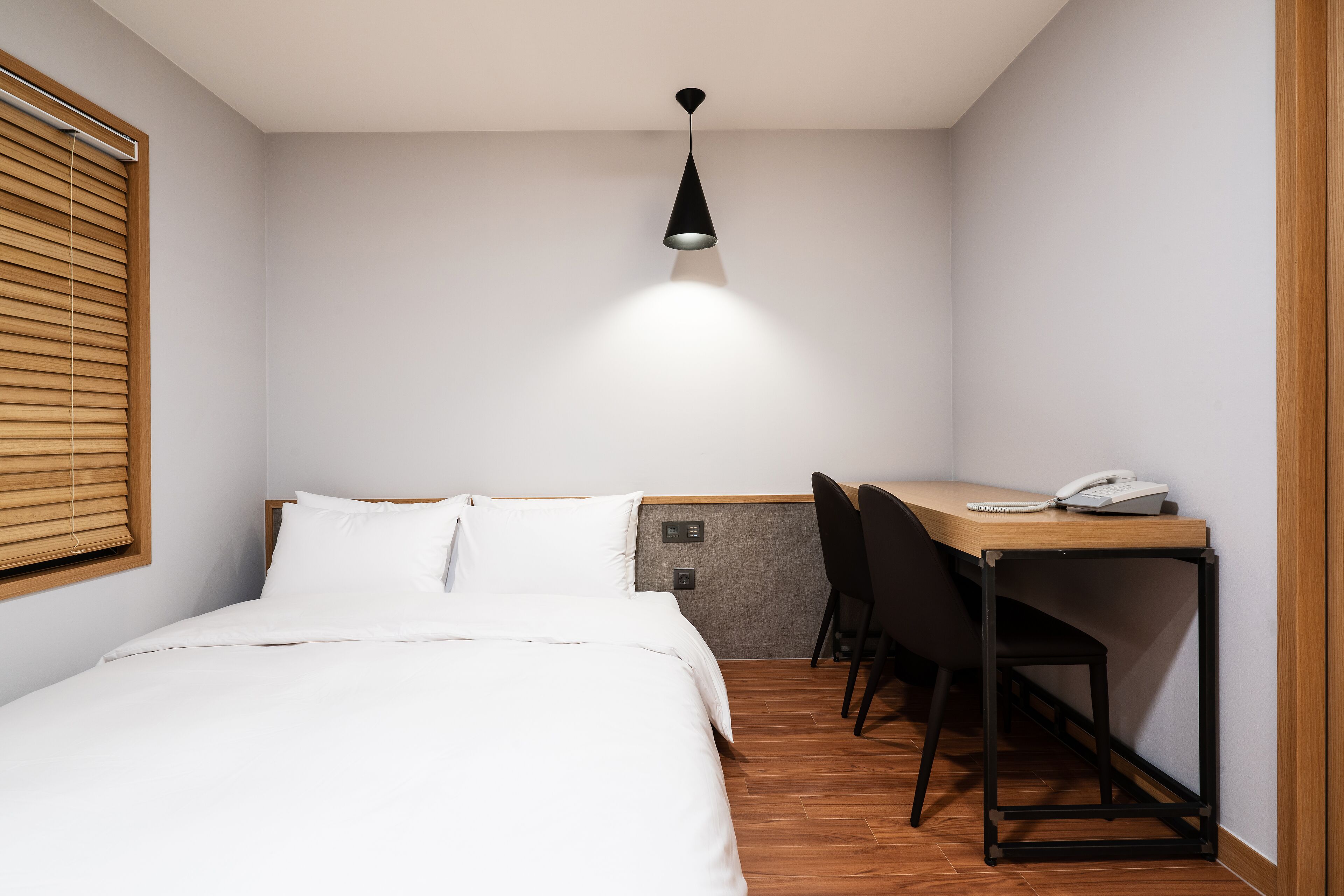 Un dormitorio con cama, escritorio y silla. Hay una lámpara en el techo sobre el escritorio.