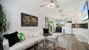 A modern living room with a glass coffee table, white sofa, and a world map artwork. - Escape to Kokomo Bay,  Escape to Paradise (Fort Myers)