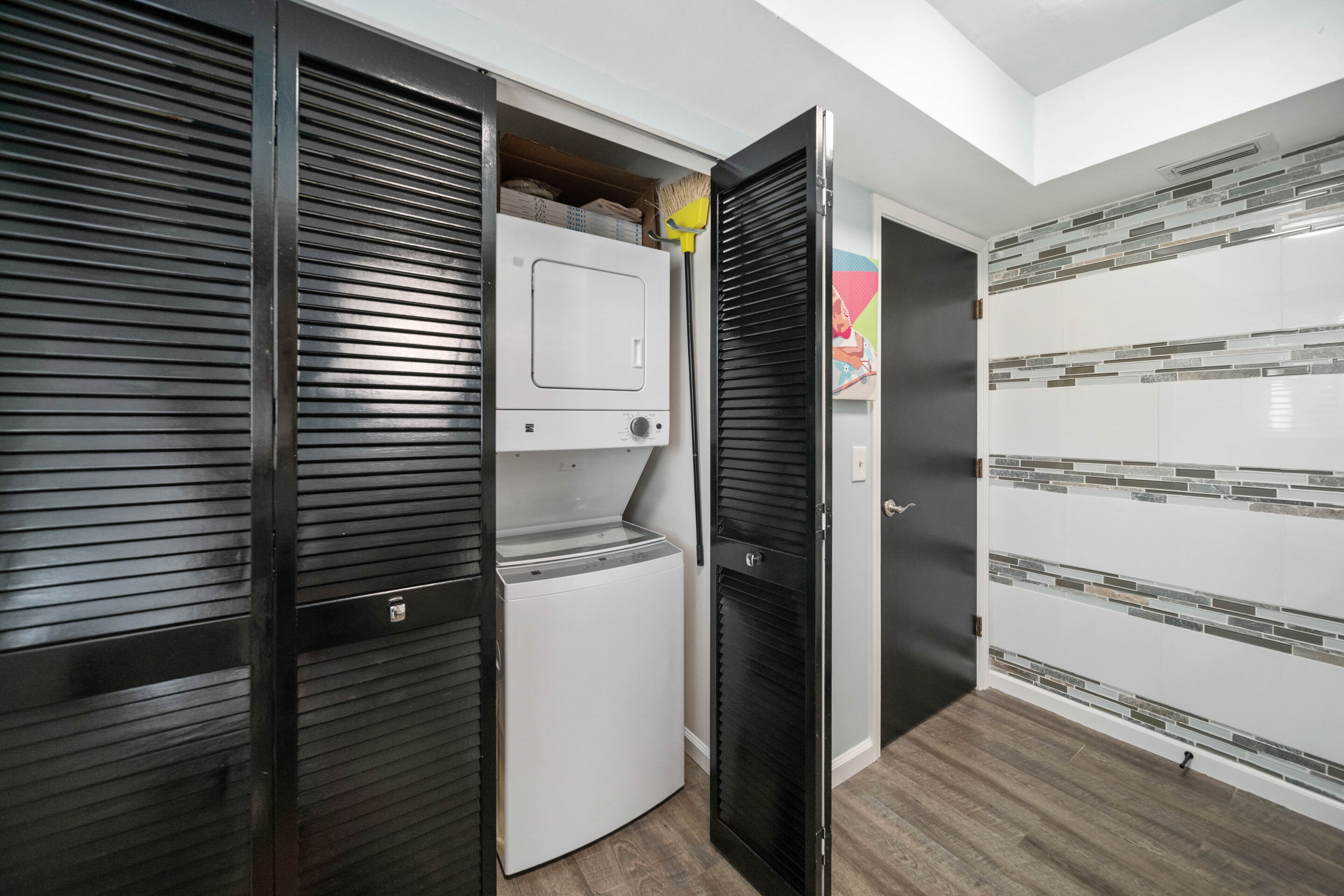 A compact room with a built-in washer and dryer, a sliding door closet, and a tiled backsplash.