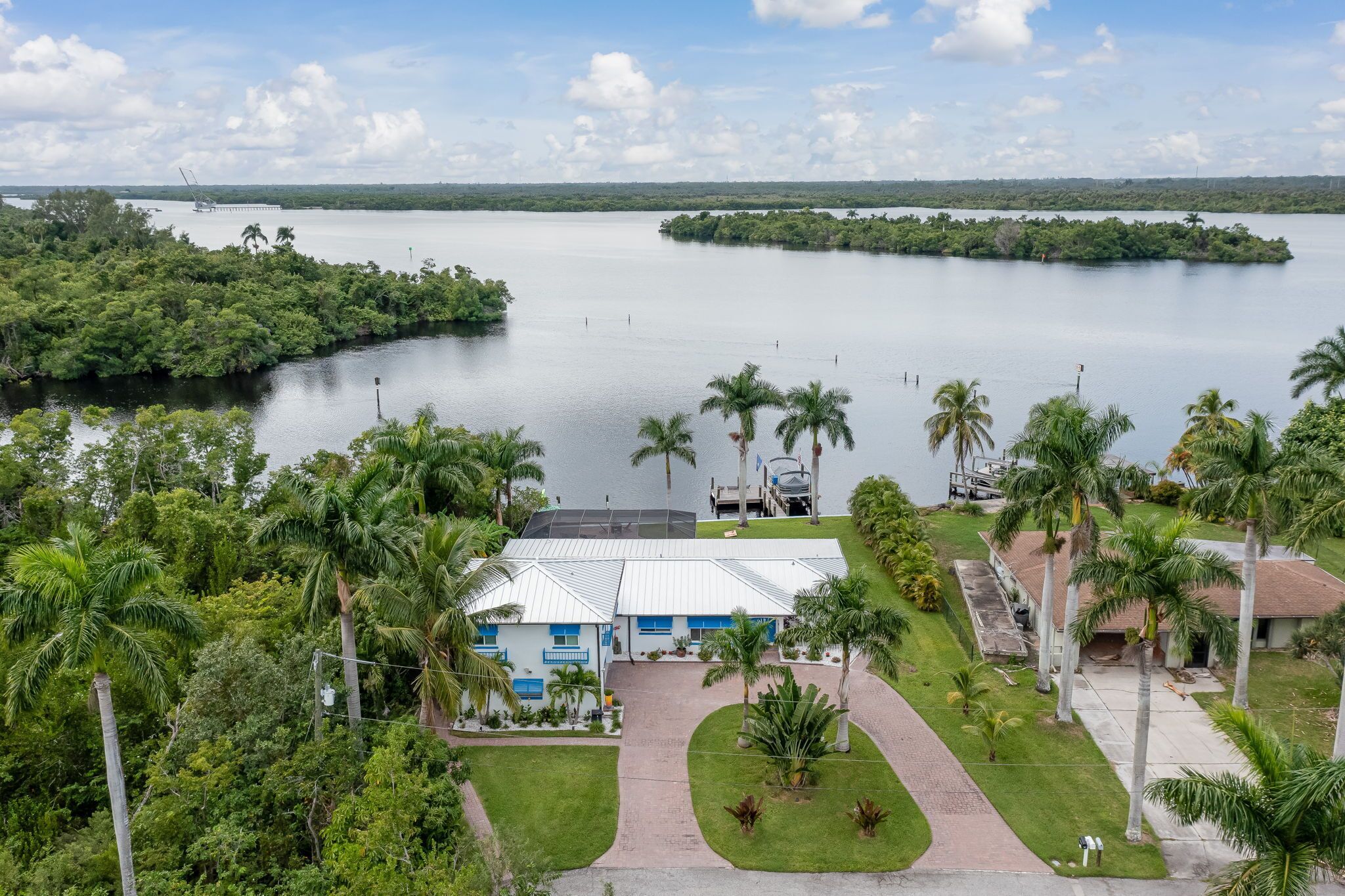 A hotel with a white building and blue accents, surrounded by lush greenery and a large body of water.