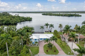 A hotel with a white building and blue accents, surrounded by lush greenery and a large body of water. - Escape to Kokomo Bay,  Escape to Paradise (Fort Myers)