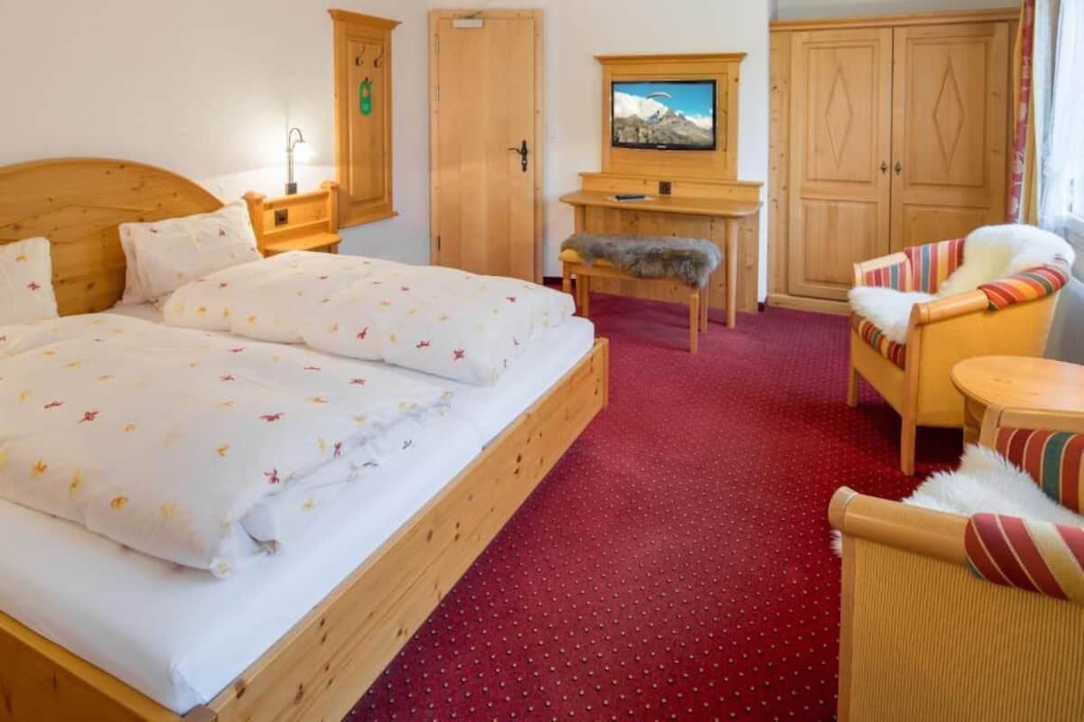 A hotel room with a large bed, a wooden desk, a television, and a wardrobe.