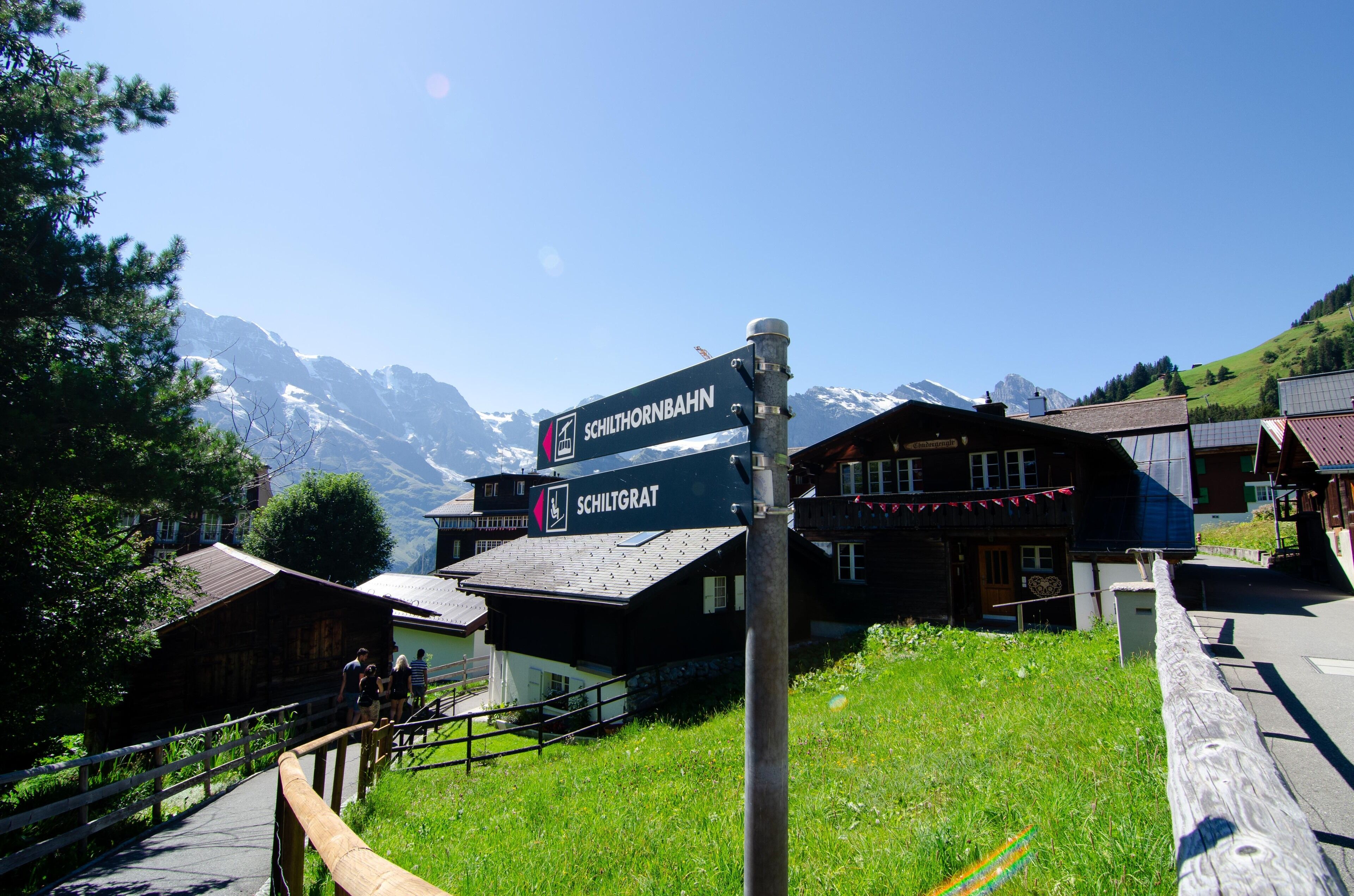 A mountain lodge with a sign indicating 'Schilthornbahn' and 'Schiltracht' paths.