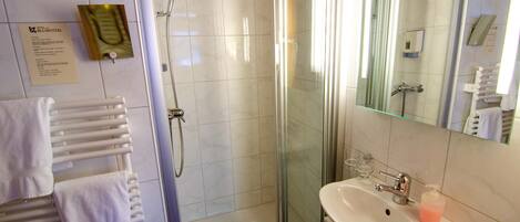 Un baño con ducha de vidrio, lavamanos blanco con dispensador de jabón y toallero con toallas blancas.