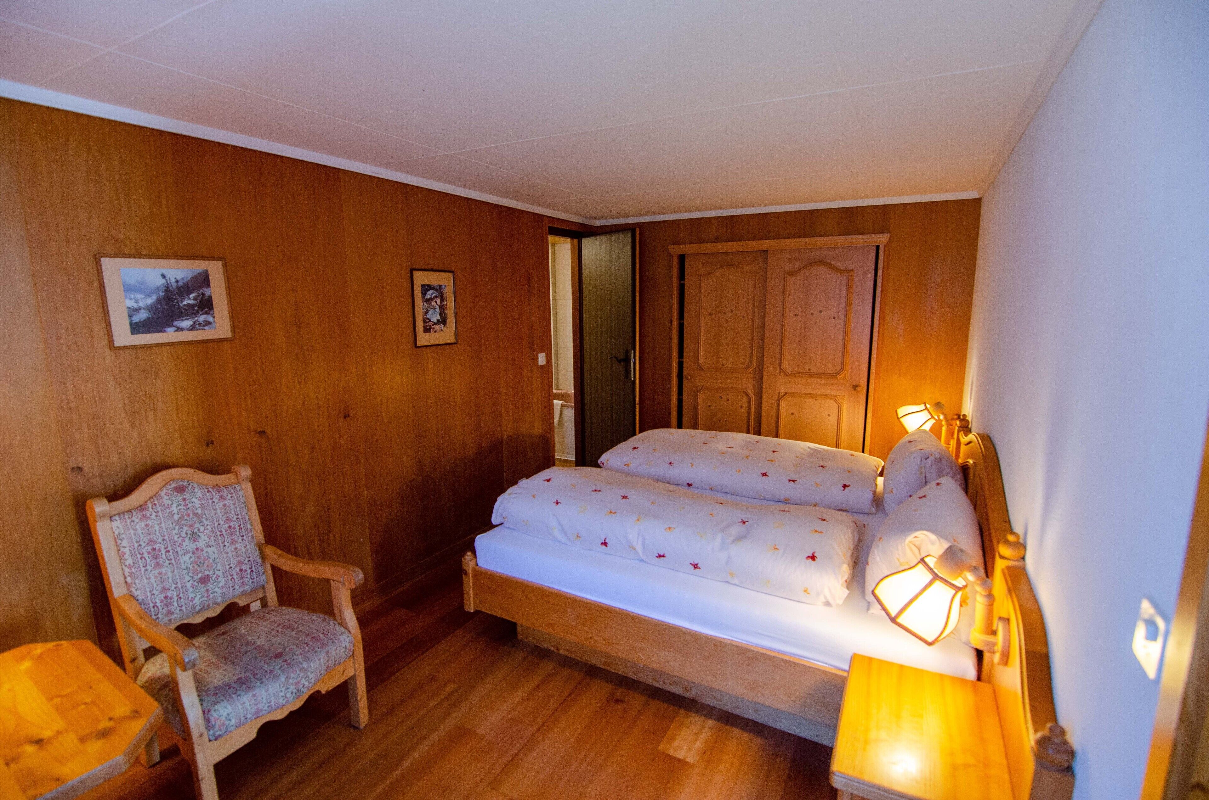 A bedroom with a wooden bed, a chair, and a small table.