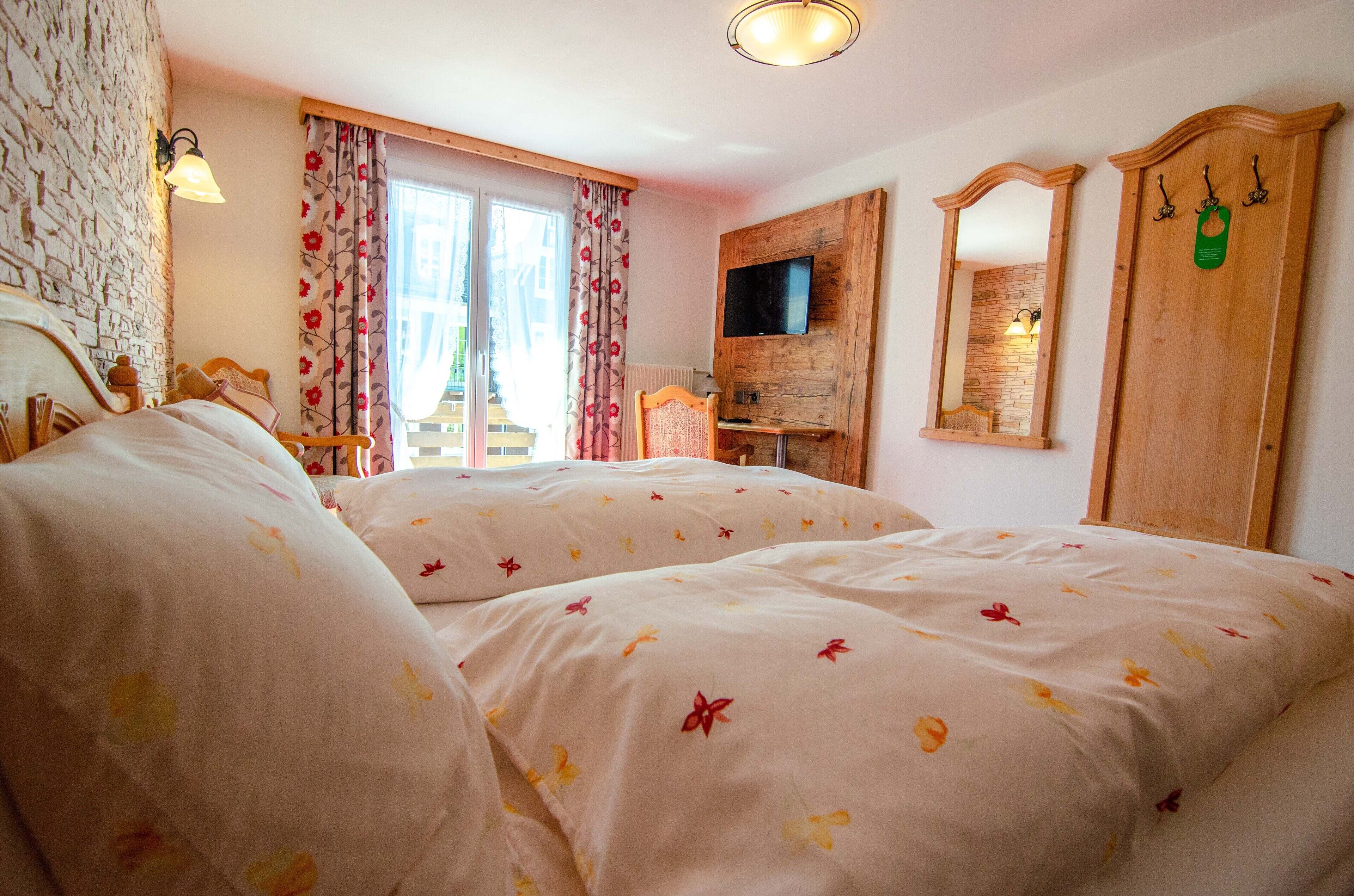 A bedroom with two beds, a TV, a wooden wardrobe, and a mirror.